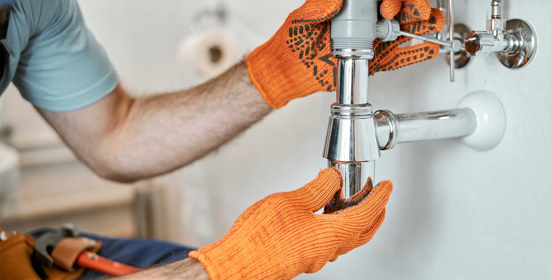 Plumber tightening a metal drain pipe beneath a sink