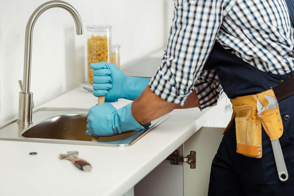 Plumber using a plunger to clear a kitchen sink drain
